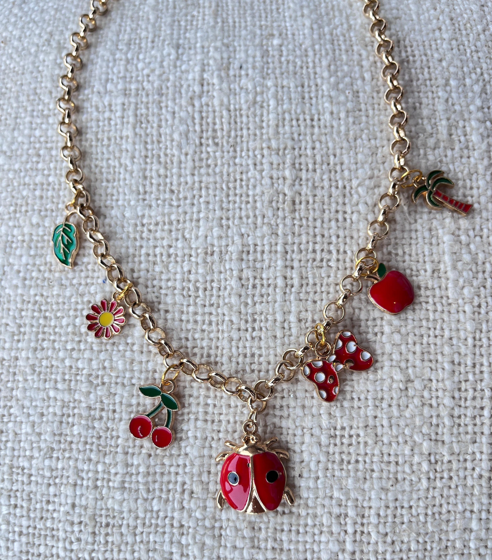 gold charm necklace with lady bug, apple, butterfly, flower, leaf, palm tree